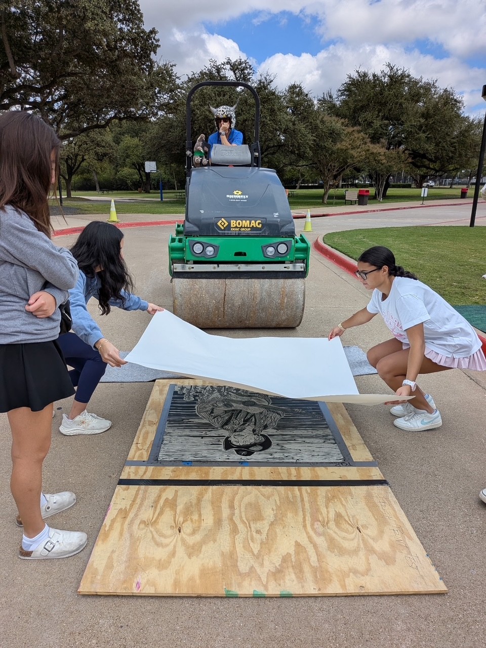 Students prepare a large print beside a steamroller at an outdoor printmaking event.